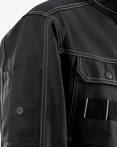 Eine Nahaufnahme einer dunkel gefärbten Jacke mit einer geknöpften Tasche, die kontrastierende Nähte und ein Riemendetail aufweist und damit ihre Designelemente hervorhebt.