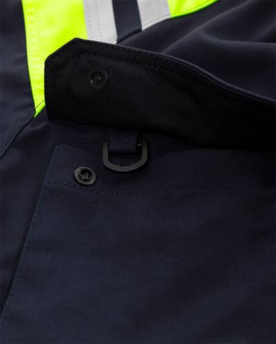 Nahaufnahme einer dunkelblauen Jacke mit neongelber Akzentuierung und einem schwarzen Knopf, mit Fokus auf den Taschenbereich und angebrachte Hardwaredetails.