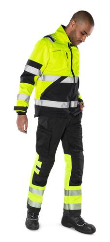 Eine Person, die eine Warnschutzkleidung mit Jacke und Hose trägt, die grelle gelbe Farbe und reflektierende Streifen aufweist, steht vor einem schwarzen Hintergrund.