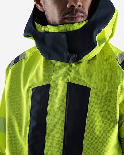 Eine Person, die eine hochsichtbare gelbe Jacke mit dunklen Reflektionsstreifen trägt, mit teilweise geschlossenem Reißverschluss und hohem Kragen.