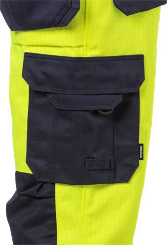 Ein Paar helle gelbe Arbeitshosen mit einer dunkelblauen, rechteckigen Tasche mit Klappe und einem Knopf an der Seite.
