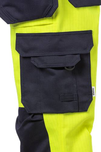 Eine Nahaufnahme einer dunklen Tasche auf hellgelbem Stoff, wahrscheinlich Teil eines Kleidungsstücks, die den Kontrast der Farben und das Design der Tasche hervorhebt.