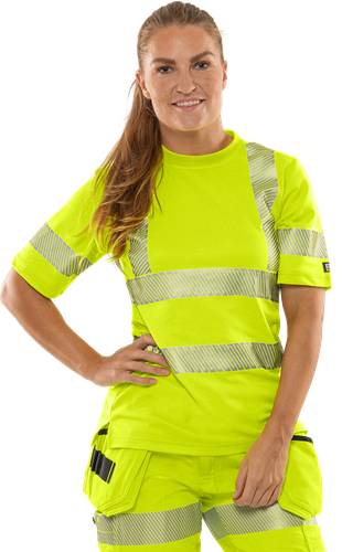 Eine Person in einem signalgelben Sicherheitshemd mit reflektierenden Streifen lächelt vor einem dunklen Hintergrund.