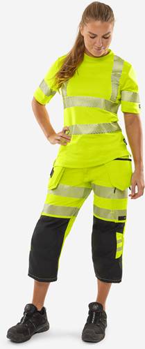 Eine Person in gelber und schwarzer Warnschutzkleidung mit reflektierenden Streifen, die vor einem neutralen Hintergrund posiert.