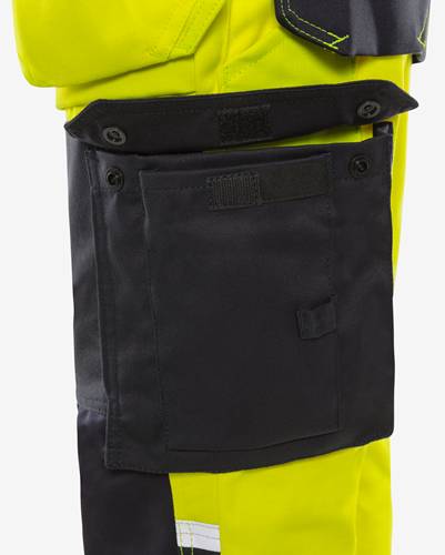 Eine schwarze Utility-Tasche mit Knöpfen ist an einem hellen gelben Kleidungsstück, höchstwahrscheinlich Arbeitskleidung, befestigt, die dazu dient, Werkzeuge oder Zubehör zu tragen.