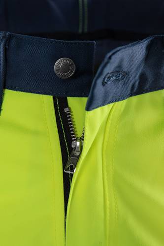 Nahaufnahme einer neongelben Jacke mit einem schwarzen Reißverschluss, einem Metallknopf mit der Aufschrift ‚CANVAS' und einem teilweise sichtbaren Kragen mit einem kleinen bestickten Logo.