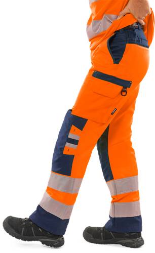 Eine Person, die eine leuchtend orange Warnschutz-Arbeitshose mit reflektierenden Streifen trägt, teilweise sichtbar, vor einem einfarbigen schwarzen Hintergrund.