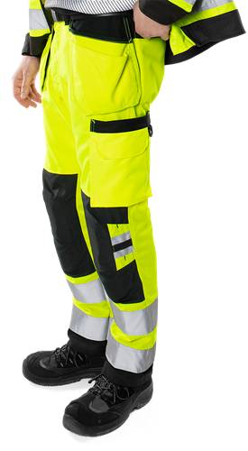 Eine Person trägt hochsichtbare gelbe und schwarze Sicherheitshosen mit reflektierenden Streifen, wobei das Kleidungsstück in seiner Sichtbarkeitsgestaltung präsentiert wird.