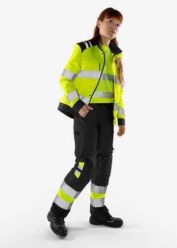 Eine Person, die eine reflektierende gelb-schwarze Uniform trägt und steht. Die Kleidung umfasst eine Warnweste mit reflektierenden Streifen.