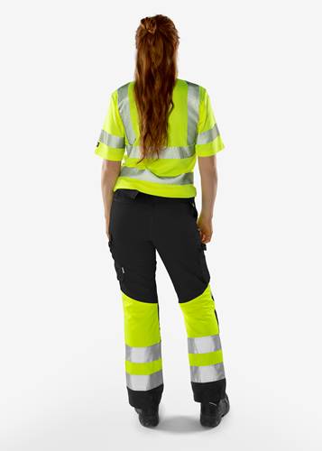 Eine Person, die eine hochsichtbare gelbe Warnweste und Hose mit reflektierenden Streifen trägt, steht mit dem Rücken zur Kamera vor einem neutralen Hintergrund.
