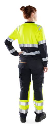 Eine Person in Arbeitskleidung mit Warnweste und reflektierenden Streifen und schwarzer Hose steht mit dem Rücken zum Betrachter.