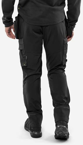 Eine Person, die schwarze Cargohosen mit mehreren Taschen trägt und aufrecht vor einem einfarbigen Hintergrund steht.