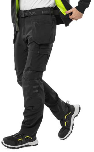 Eine Person, die schwarze taktische Hosen mit verstärkten Knien und mehreren Taschen trägt, steht vor einem dunklen Hintergrund.