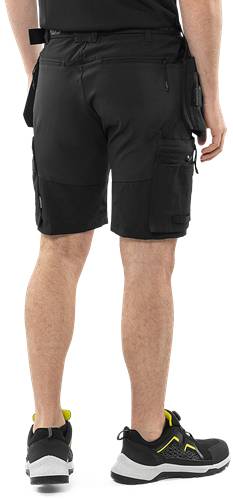 Rückansicht einer Person, die schwarze Cargo-Shorts trägt, mit mehreren Taschen, vor einem schwarzen Hintergrund.