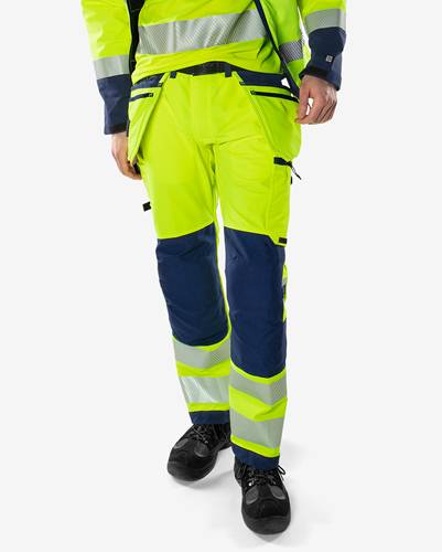 Eine Person, die leuchtend gelbe und marineblau-farbene Arbeitshosen mit reflektierenden Streifen trägt, was Sicherheitskleidung für Bau- oder Industriearbeit andeutet.