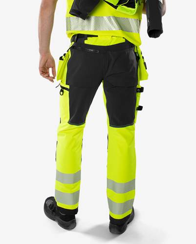 Eine Person, die von hinten gesehen eine reflektierende Warnschutz-Arbeitshose trägt. Die Hose ist gelb und schwarz mit reflektierenden Streifen.