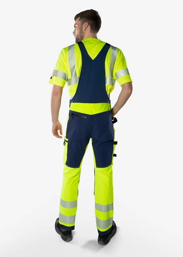Eine Person trägt hochsichtbare Arbeitskleidung, darunter eine gelbe und marine-blaue Arbeitsmontur mit reflektierenden Streifen, von hinten gegen einen einfarbigen Hintergrund gesehen.