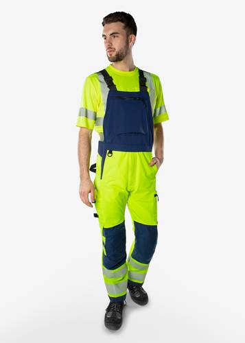 Eine Person, die leuchtend gelbe und blaue Warnschutz-Arbeitsoveralls mit reflektierenden Streifen trägt, vor einem einfarbigen Hintergrund.