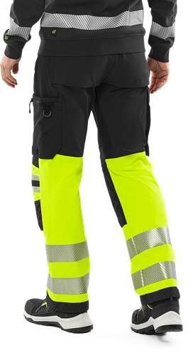 Person trägt hochsichtbare gelbe und schwarze Arbeitshose mit reflektierenden Streifen.