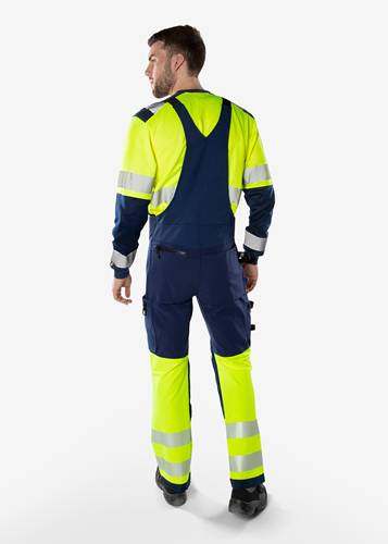 Eine Person, die Arbeitskleidung mit Warnfarben und reflektierenden Streifen trägt, von hinten zu sehen, geeignet für Außen- oder industrielle Umgebungen.