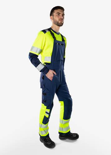 Eine Person trägt einen Arbeitsschutzanzug in Signalgelb und Dunkelblau mit reflektierenden Streifen an den Ärmeln und Hosenbeinen.
