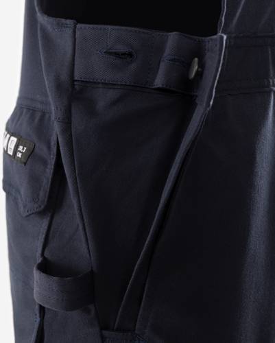 Nahaufnahme eines marineblau-farbenen Hosenstoffs mit einer seitlichen Tasche, die eine Knopfdetail und ein kleines schwarz-weißes Etikett auf der Taschenlasche aufweist.