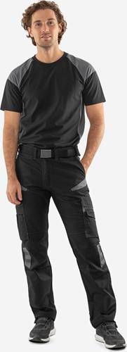 Eine Person steht mit einer schwarzen T-Shirt und schwarzer Cargo-Hose, wobei die Hände seitlich am Körper hängen, mit Fokus auf die untere Körperhälfte und Kleidungsdetails.