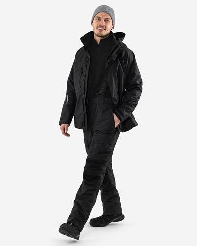 Eine Person in schwarzer taktischer Kleidung steht selbstbewusst, trägt eine Jacke, Hose und Stiefel, vor einem einfarbigen Hintergrund.