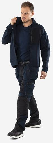 Eine Person trägt eine dunkelblaue Jacke und Cargohose mit mehreren Taschen, was typische Arbeitskleidung mit Nutzwert präsentiert.