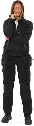 Eine Person, die schwarze Taktische Hosen mit mehreren Taschen und eine schwarze Jacke trägt, von der Hüfte abwärts gezeigt, vor einem dunklen Hintergrund.