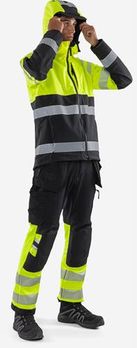 Eine Person, die eine schwarz-graue Warnschutzjacke und Hose mit reflektierenden Streifen trägt, aus der Rückansicht.