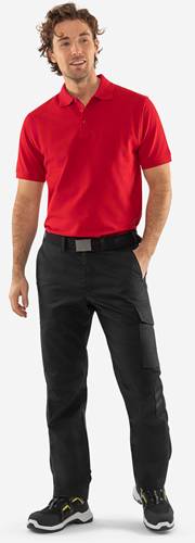 Eine Person in einem roten Poloshirt, das in eine schwarze Hose gesteckt ist, steht vor einem neutralen Hintergrund.