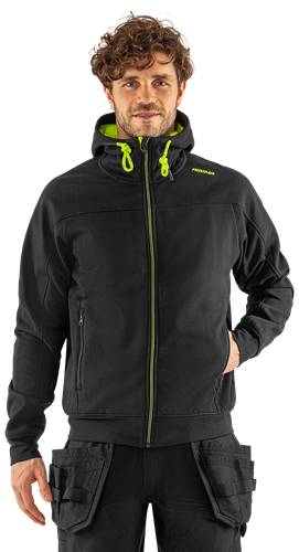 Eine Person, die eine schwarze Jacke mit grünem Reißverschluss und Kapuzendetails trägt, vor einem schwarzen Hintergrund.