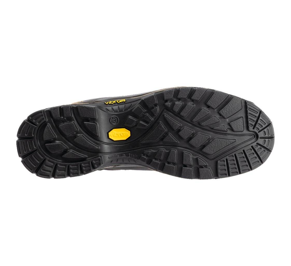 Das Bild zeigt die Sohle eines Schuhs mit einem groben, strukturierten Muster, das für Traktion konzipiert ist. Die Sohle ist überwiegend schwarz mit einem kleinen gelben Etikett.