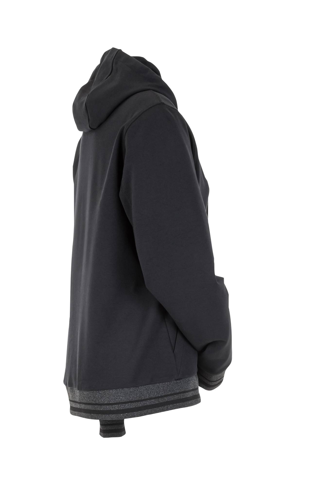 Eine Person mit einer schwarzen Kapuzenjacke, seitlich ausgerichtet und die Hände in den Taschen, vor einem einfarbigen Hintergrund.