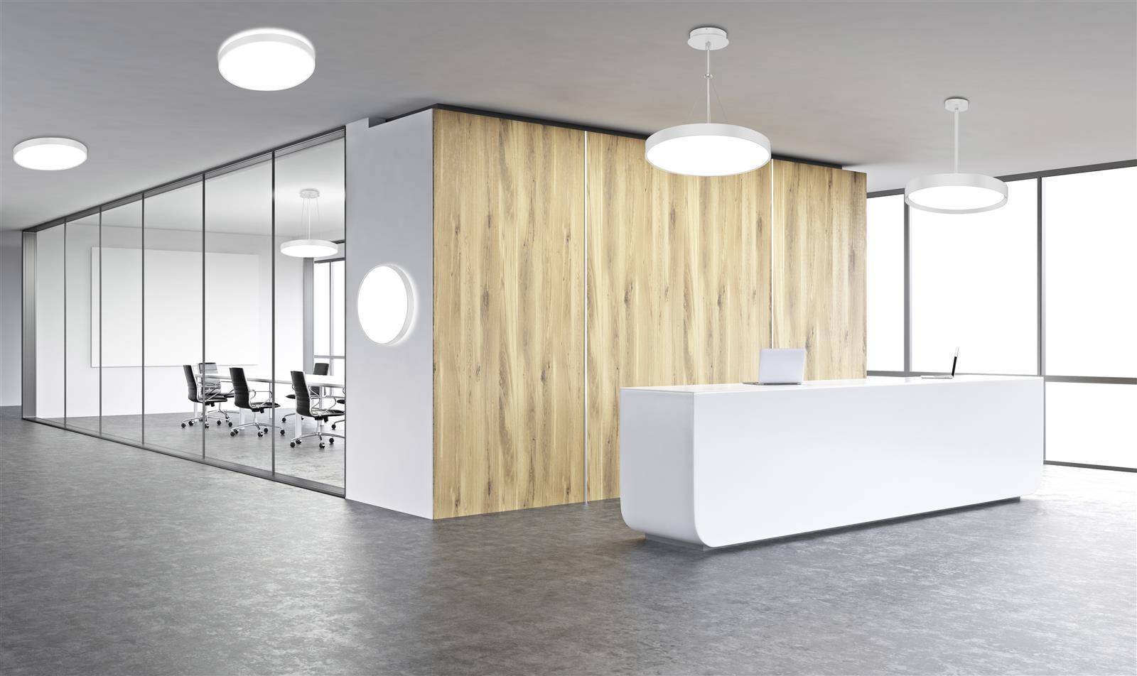 Eine moderne Bürolobby mit einem elegantem weißen Empfangstresen vor Holzvertäfelung. Ein gläserner Besprechungsraum mit Stühlen ist zu sehen.