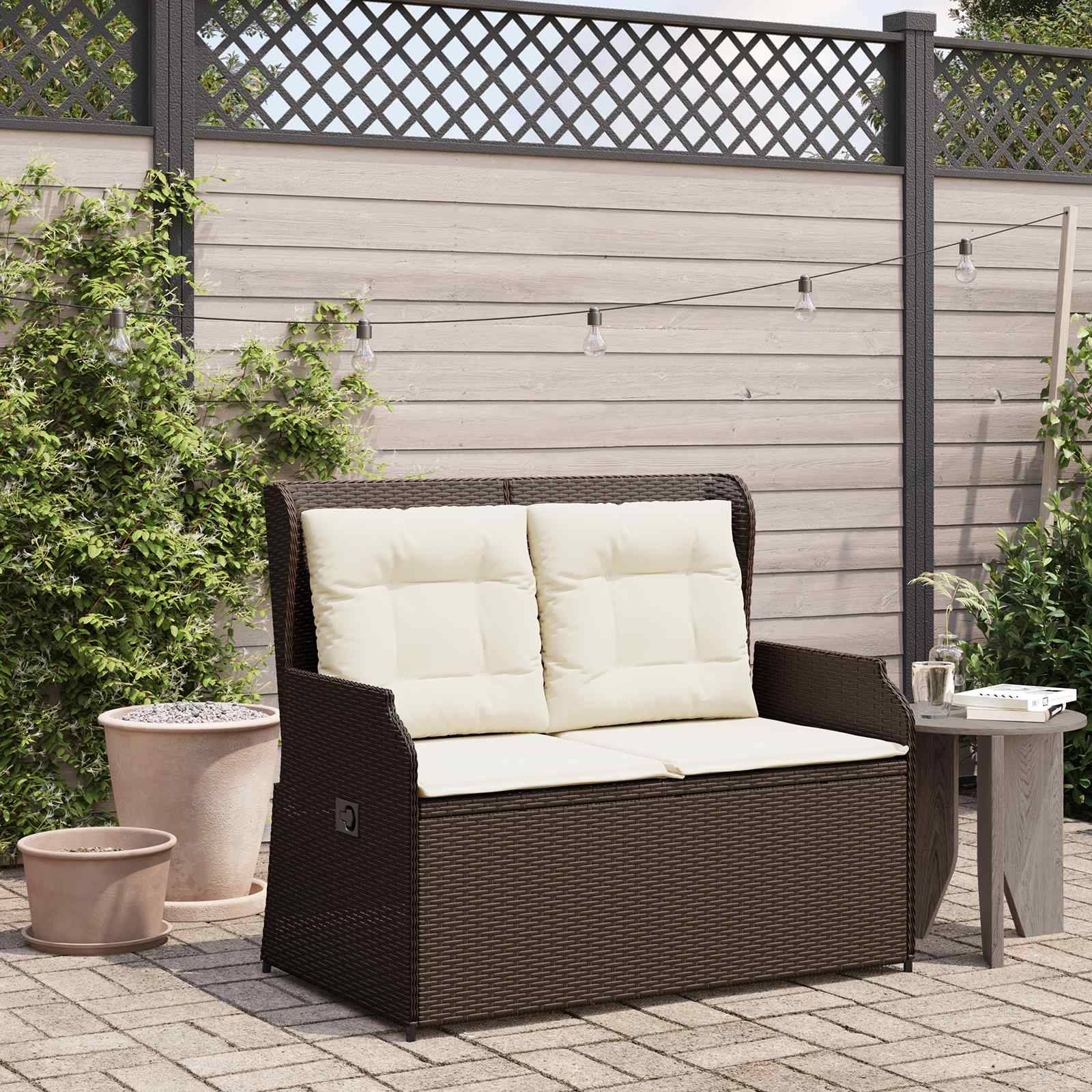Outdoor-Terrassenszenerie mit einer Flechtwerk-Sitzbank mit cremefarbenen Kissen, die auf einem gefliesten Boden steht. Lichterketten hängen darüber, und Topfpflanzen umgeben die Sitzbank.
