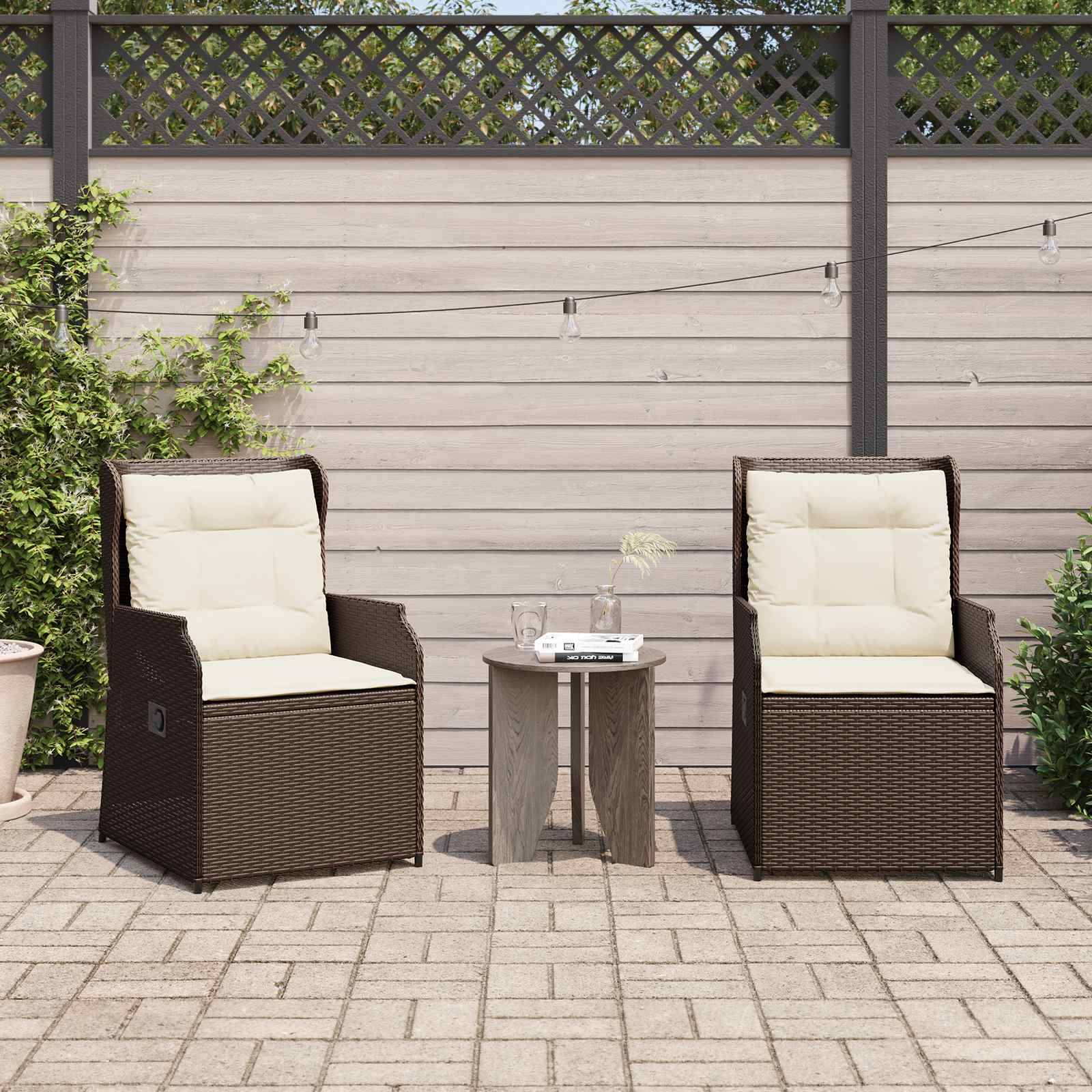 Zwei Korbstühle mit beigen Kissen auf einer Terrasse, getrennt durch einen kleinen Holztisch mit einer Weinflasche und Gläsern, unter Lichterketten.