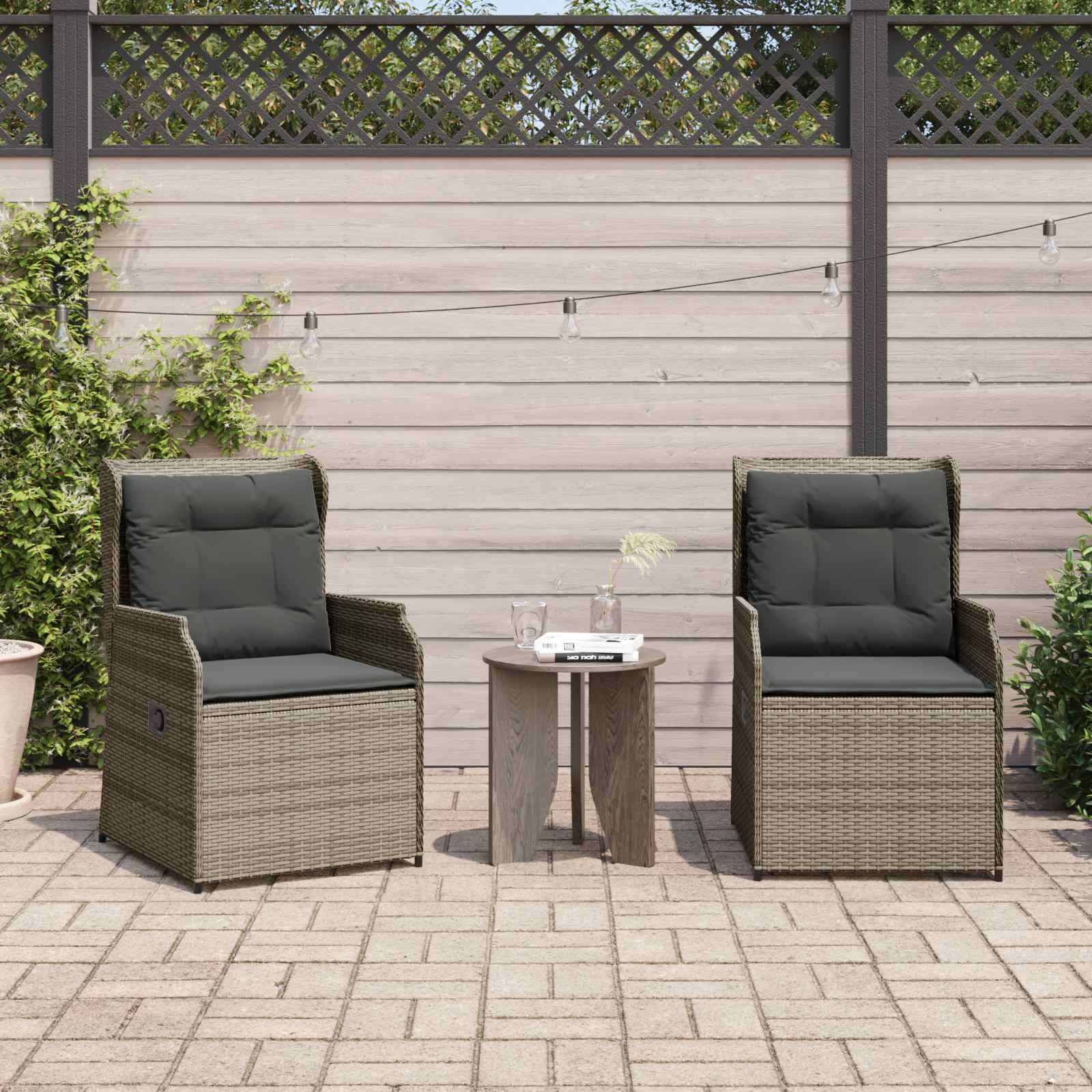 Zwei Korbstühle mit schwarzen Kissen stehen sich auf einer Terrasse gegenüber, zwischen ihnen steht ein kleiner runder Tisch. Im Hintergrund befindet sich ein Holzzaun und Lichterketten.
