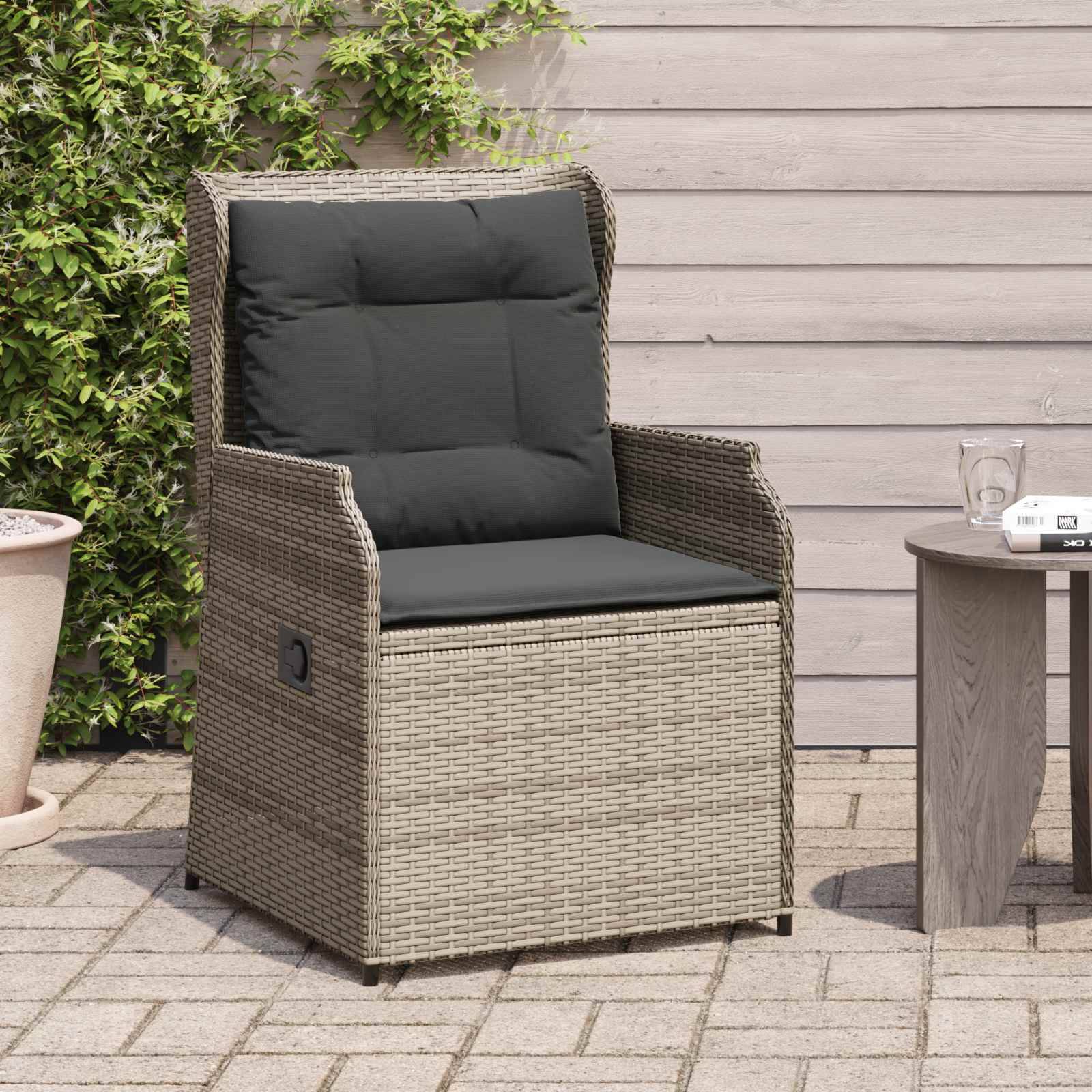 Outdoor-Rattanstuhl mit dunklen Kissen steht auf gepflasterter Terrasse neben einem kleinen runden Tisch mit einem Glas und einer weißen Tasse. Grünpflanzen im Hintergrund.