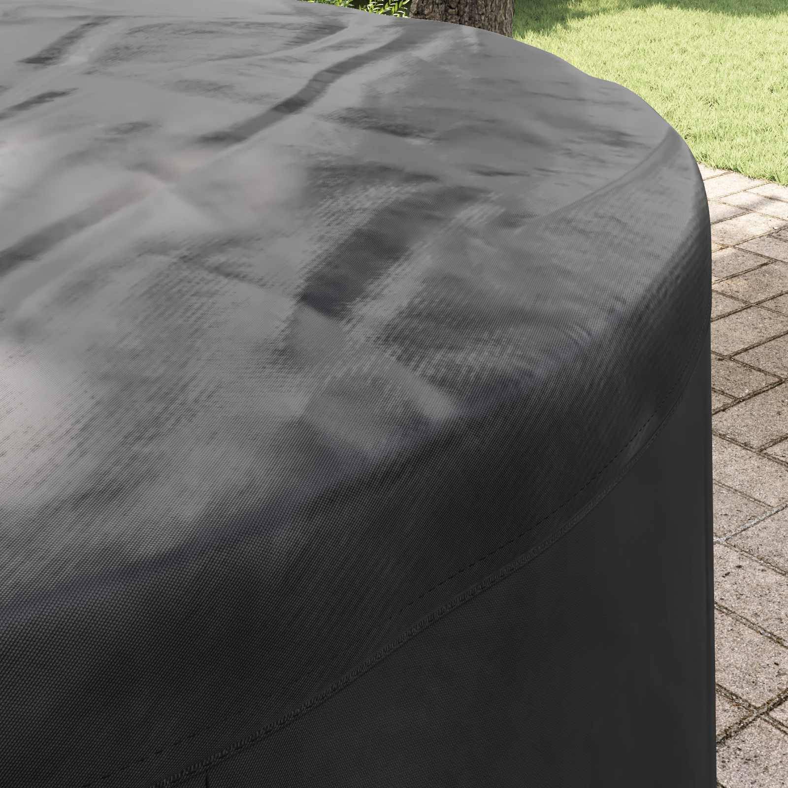 Eine große, schwarze, wetterfeste Abdeckung, die ein rundes Outdoor-Objekt, wahrscheinlich ein Möbelstück, auf einer Steinterrasse neben einem Rasenbereich schützt.