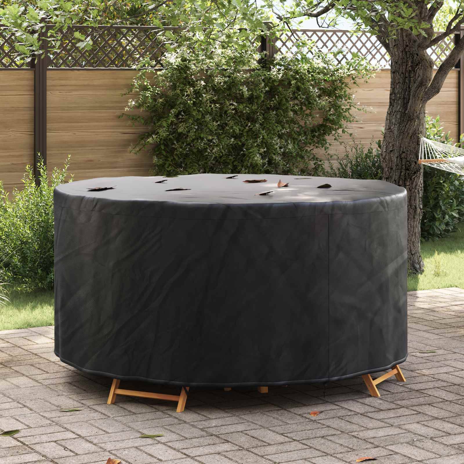 Schwarze Grillabdeckung auf einem runden Grill in einem Garten, aufgestellt auf einer Steinpterrasse mit grünem Rasen und Holzzaun im Hintergrund.