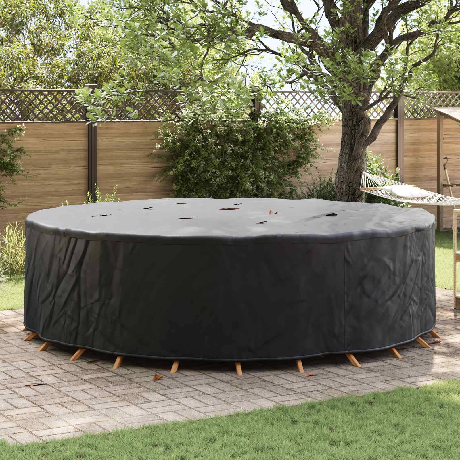 Eine runde, große Whirlpool ist mit einer schwarzen Schutzabdeckung versehen. Er steht auf einer Terrasse, umgeben von Grünpflanzen und einem Holzzaun.