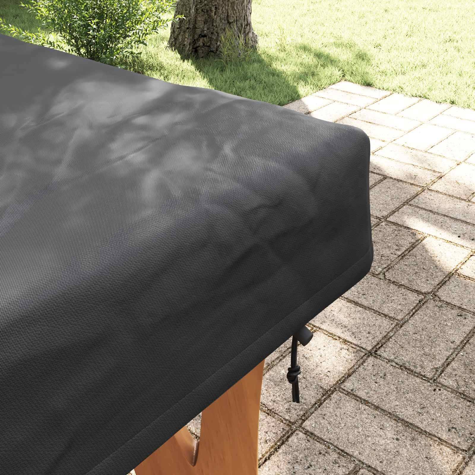 Eine schwarze Abdeckung ist über ein Stück Terrassenmobiliar an einem sonnigen Patio gelegt, mit Gras und einem Baum im Hintergrund.