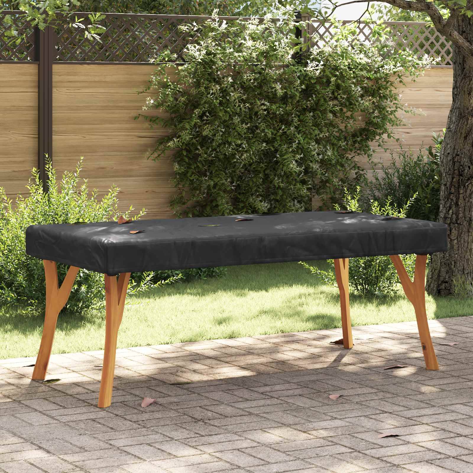 Eine schwarze Outdoor-Gartenbank mit Holzbeinen steht auf einer gepflasterten Terrasse, umgeben von grünem Gras und einem Holzzaun.