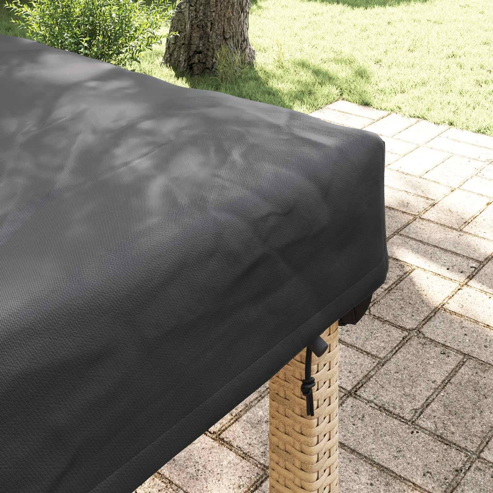 Ein Terrassentisch, der mit einer schwarzen, wetterbeständigen Abdeckung versehen ist, steht auf einer steingepflasterten Terrasse mit grünem Gras und einem Baum im Hintergrund.