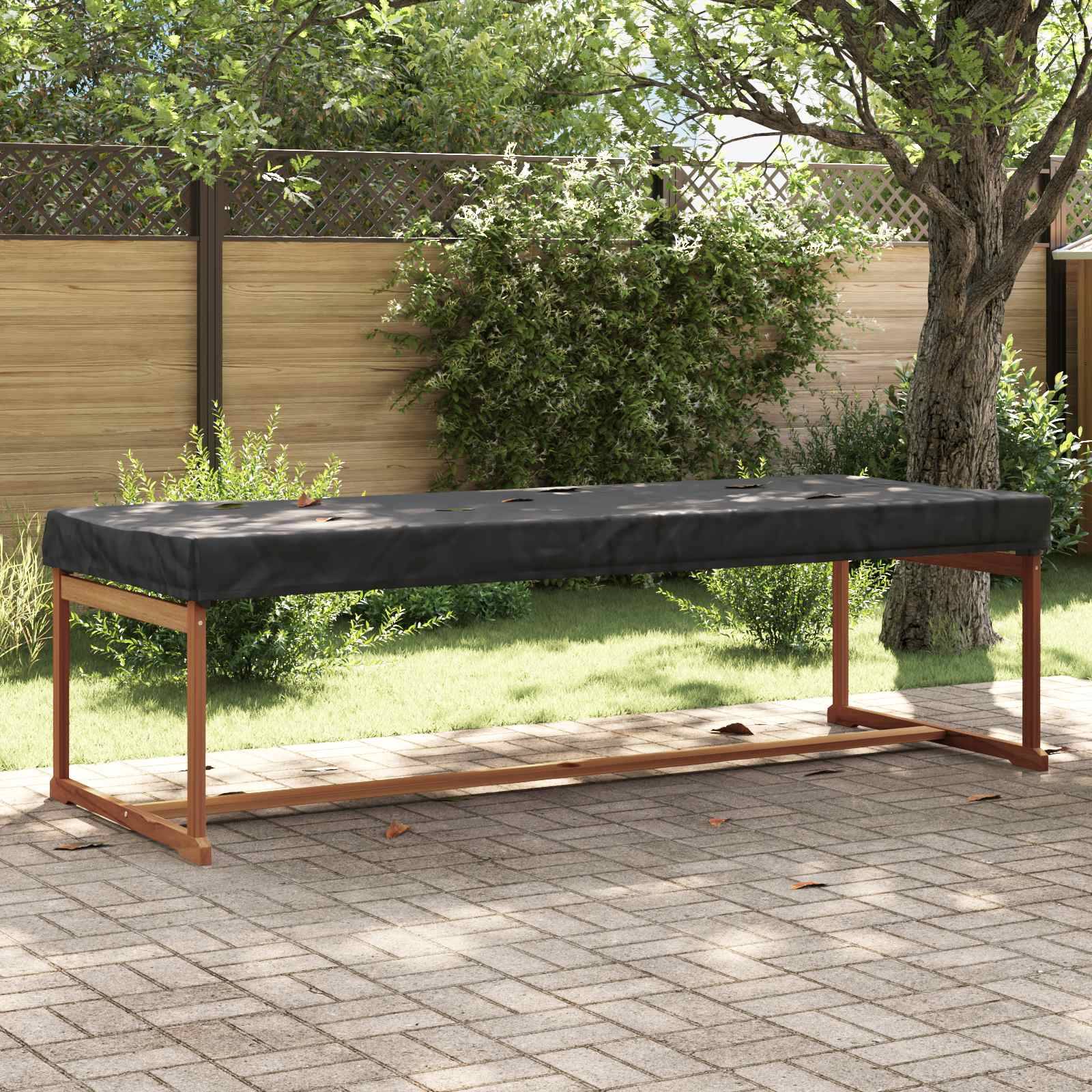 Outdoor-Tisch mit schwarzer Abdeckung, aufgestellt auf einer Steinterrasse neben Grünpflanzen und einem Holzzaun unter klarem Himmel.