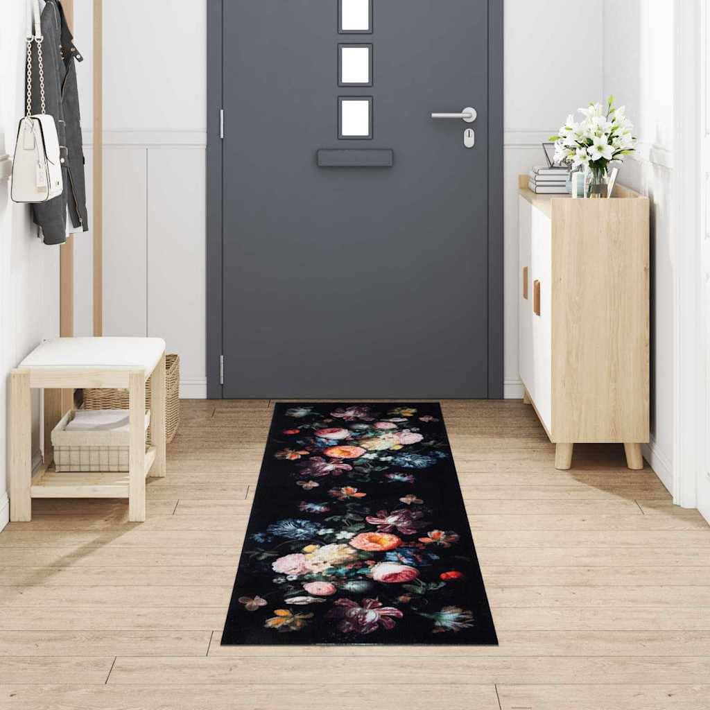 Ein Flur zeigt eine dunkelgraue Tür mit vier quadratischen Fenstern, einen Läufer mit Blumenmuster, eine kleine Holzbank auf der linken Seite und einen Schrank mit einer Pflanze auf der rechten Seite.