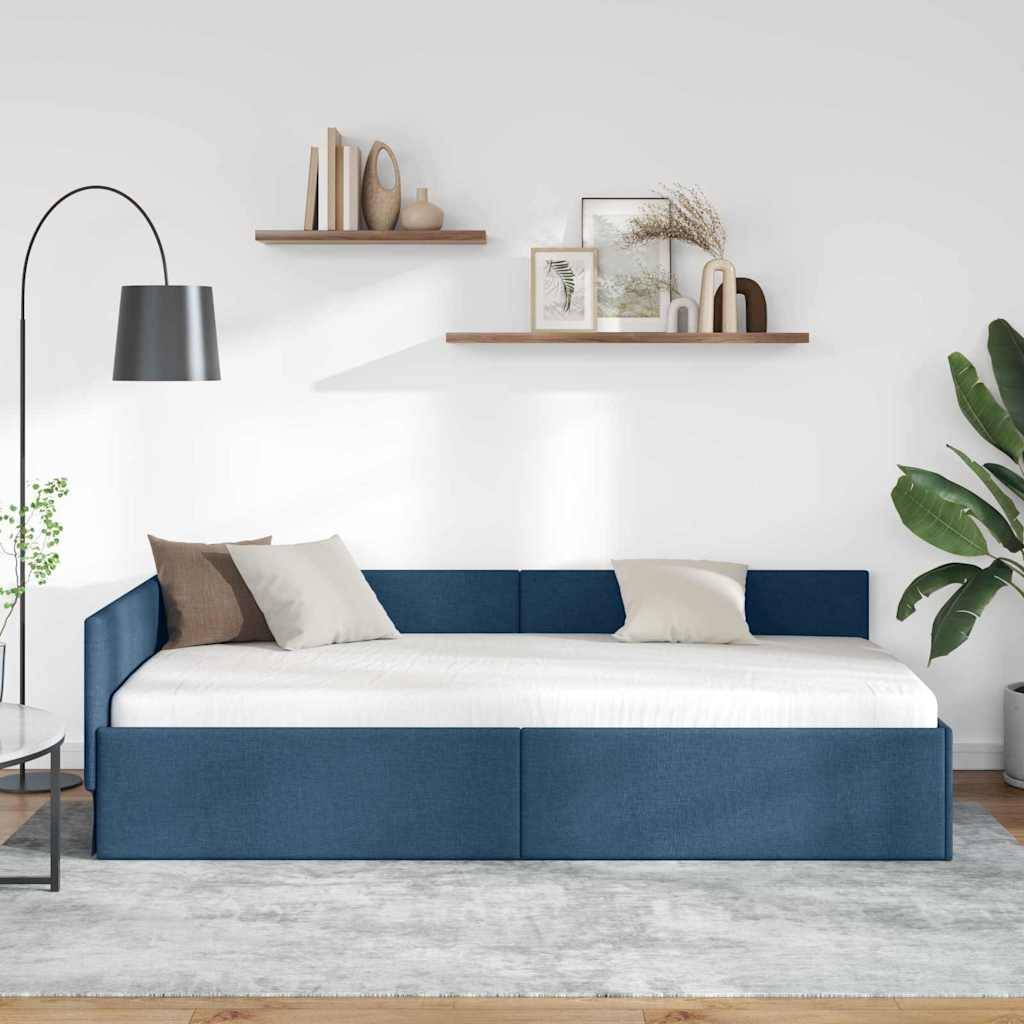 Modernes blaugepolstertes Tagesbett mit weißer Bettwäsche und Dekokissen, präsentiert vor einer weißen Wand mit Wandregalen, einer Stehlampe und Zimmerpflanzen.