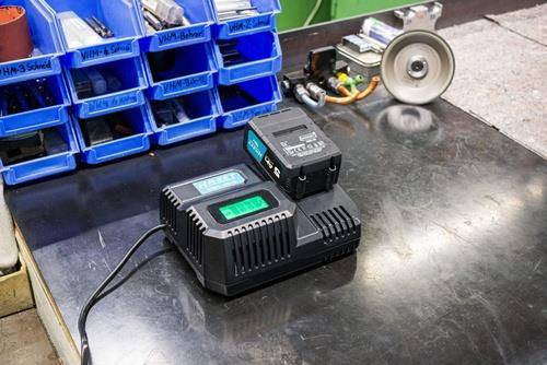 Eine Werkbank mit sortierten blauen Behältern, ein Ladegerät mit einem sich ladenden Akku und Werkzeuge, was auf eine Wartungs- oder Werkstattumgebung hindeutet.